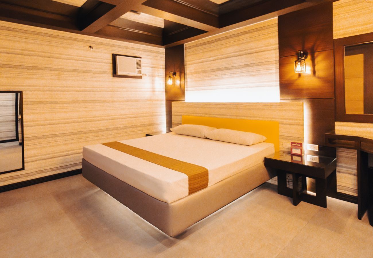 A modern hotel room with a large bed, a bedside table, and a wall-mounted lamp.