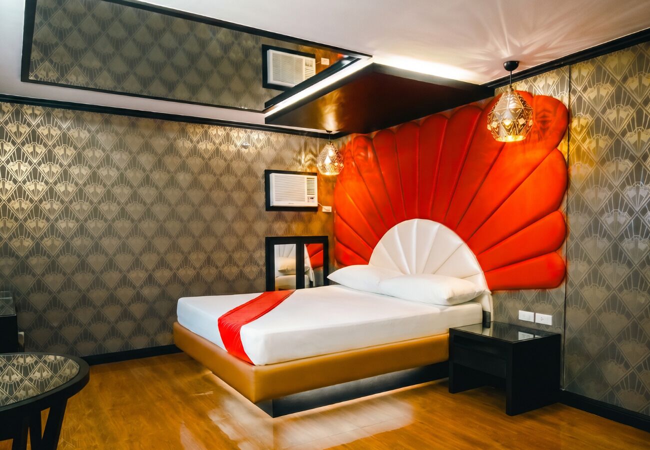 A modern hotel room with a large bed, a nightstand, a small table, and a decorative wall panel.