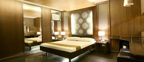 Una habitación de hotel moderna con una cama grande, dos mesitas de noche con lámparas, un espejo y un panel de pared de madera.