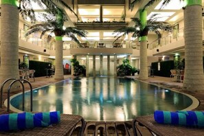 An indoor swimming pool with a central island, surrounded by lounge chairs and palm trees. - Sun Boutique Hotel (Kuta)
