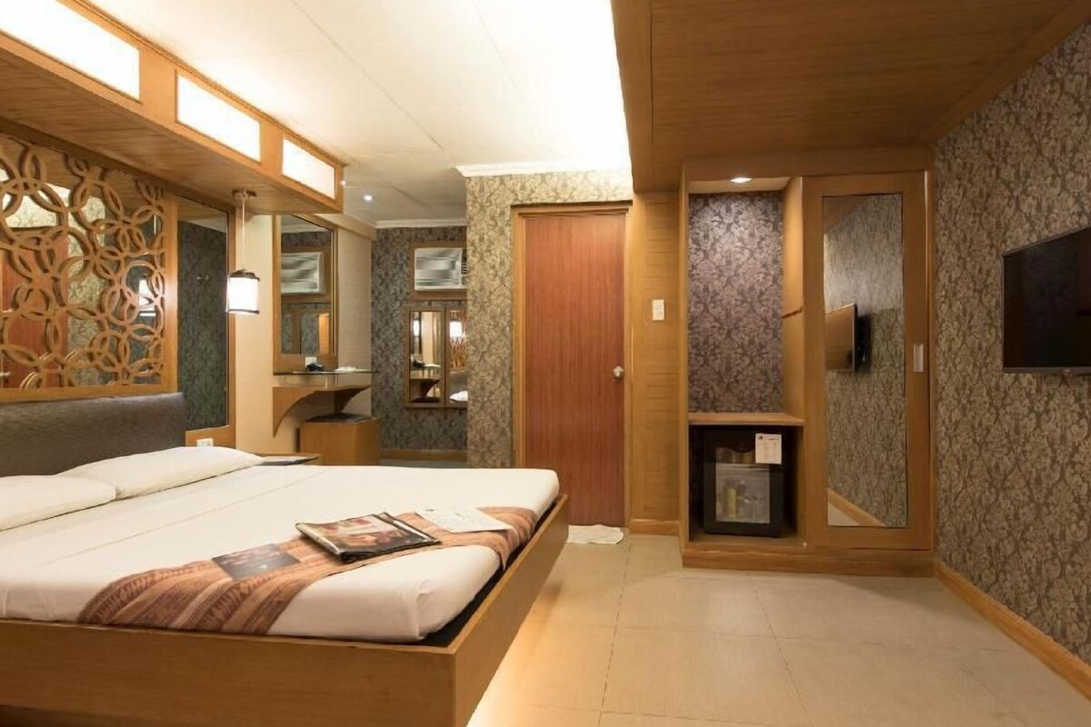 A bedroom with a bed, a vanity, a mirror, a television, and a wardrobe.