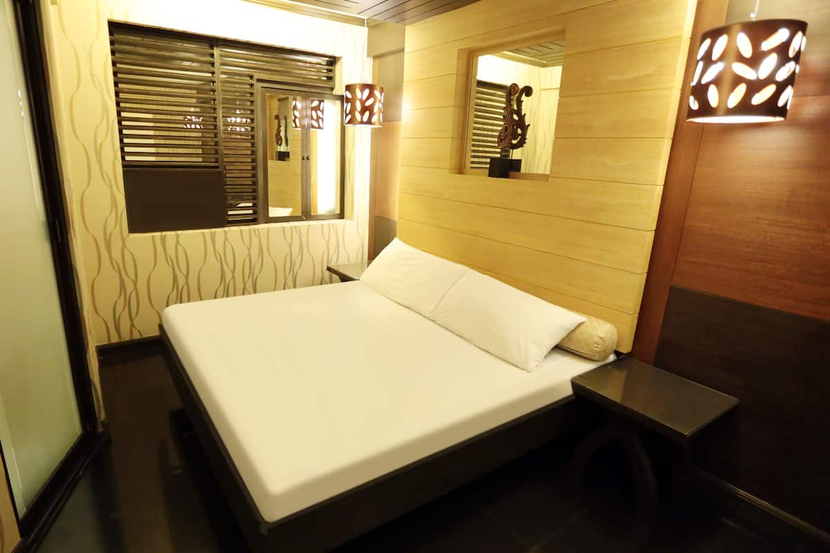 A hotel room with a bed, a bedside table, a window with blinds, and a wall-mounted mirror.