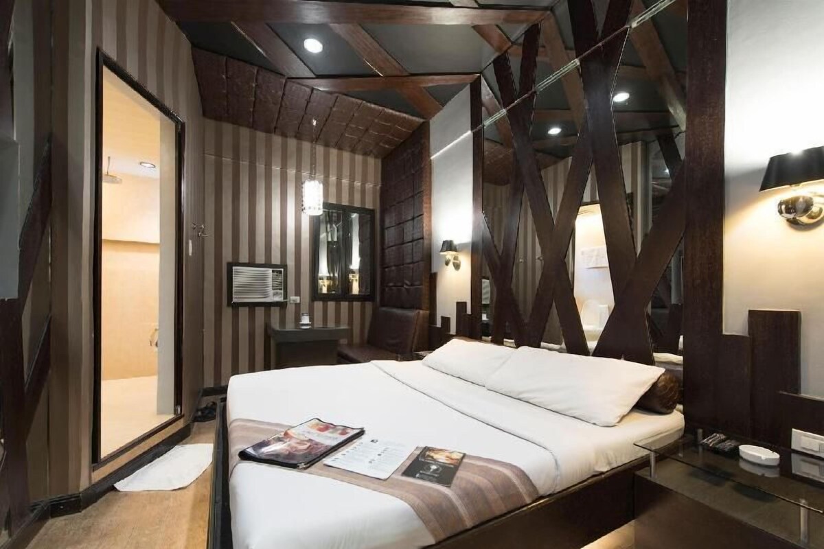 Una habitación de hotel moderna con una cama grande, una mesita de noche, un espejo y un armario.