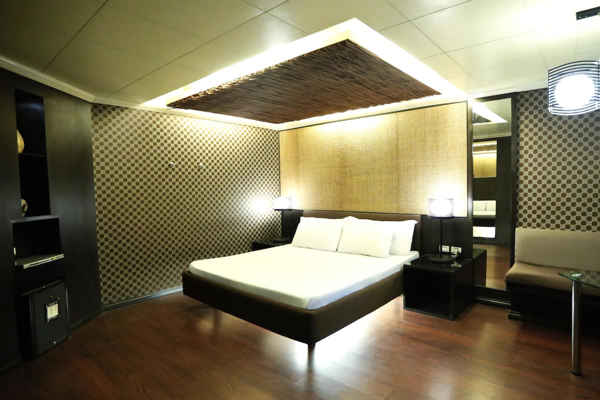 A modern hotel room with a large bed, a small desk, a chair, and a sofa.