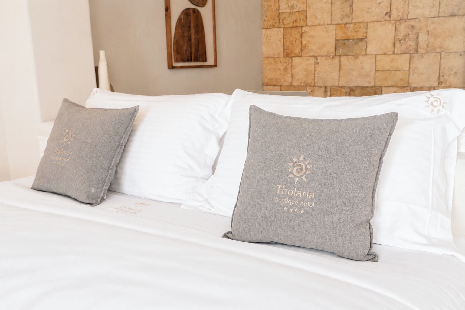Una cama con sábanas blancas y dos almohadas grises con logotipos y texto en relieve.