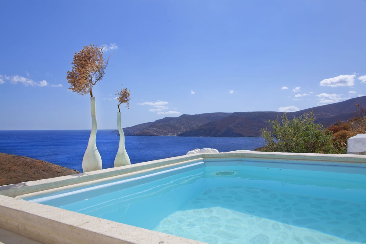 Une piscine à l’eau d’un bleu cristallin, entourée de vases blancs, avec vue sur la mer et les collines.
