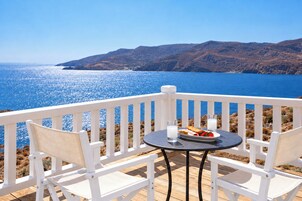 Una terraza con sillas blancas y una mesa, con vistas a un cuerpo de agua y colinas.