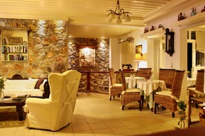 Una habitación acogedora con pared de piedra, una estantería, un sillón blanco, sillas de mimbre y una mesa de comedor.