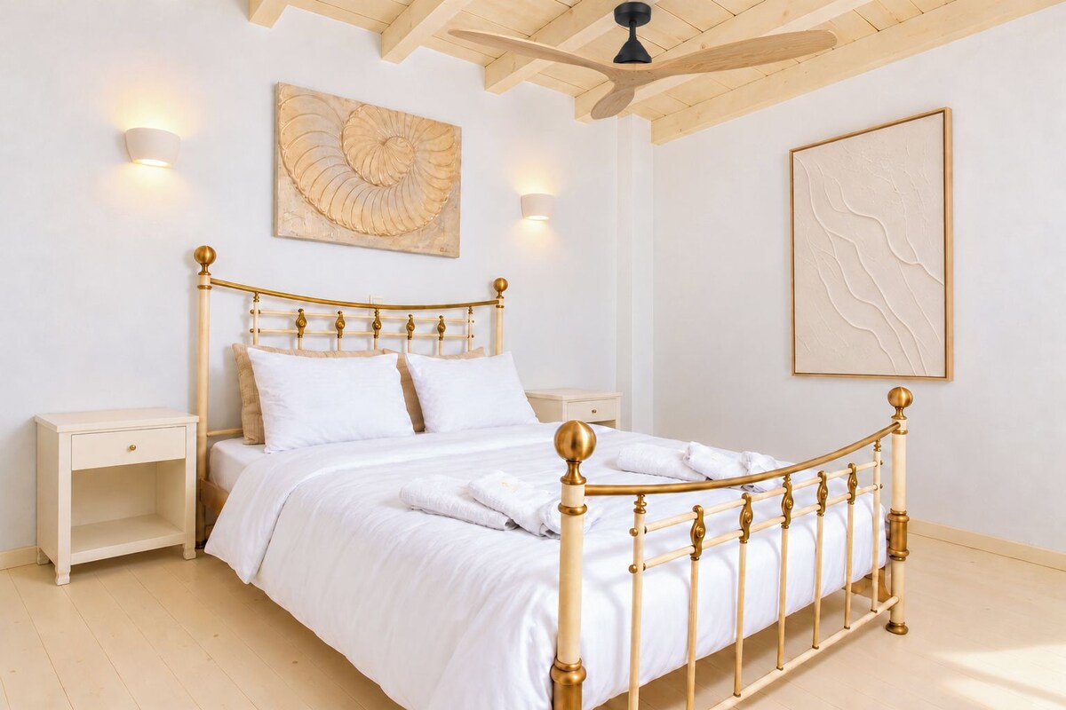 Una cama con estructura de madera y detalles dorados, una mesita de noche, una lámpara de pared y un ventilador de techo.