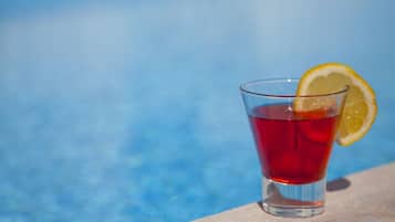 A glass of red beverage with a lemon slice garnish, placed on a ledge by a pool.