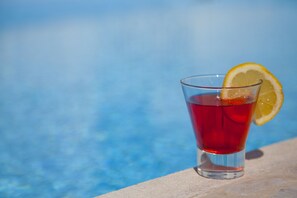 A glass of red beverage with a lemon slice garnish, placed on a ledge by a pool. - Tholaria Boutique Hotel (Astypalaia)