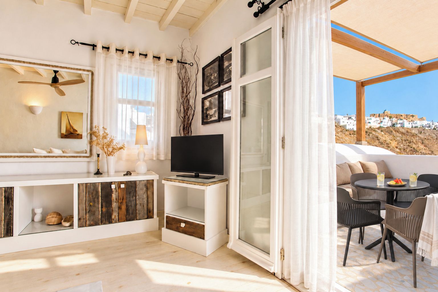 A modern living room with a television, a dining area with outdoor seating, and a view of a coastal landscape.
