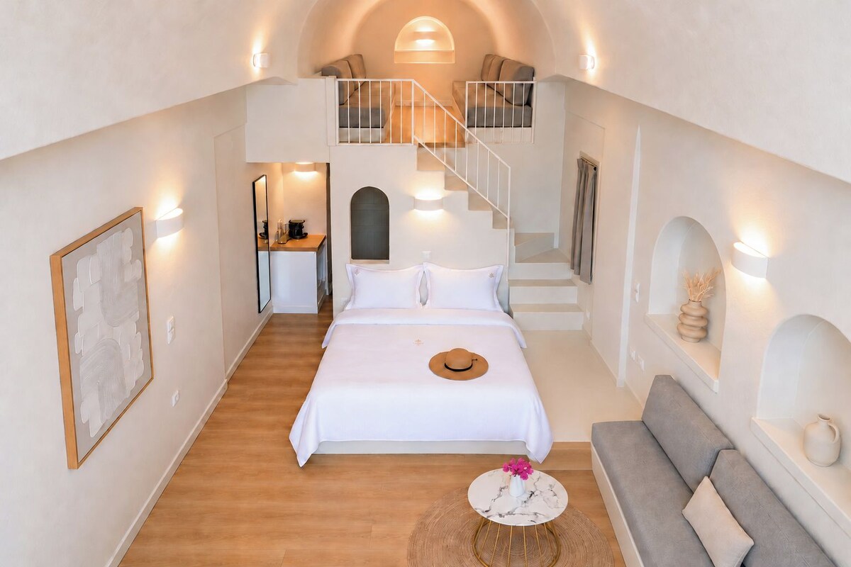 Un dormitorio con una cama, una mesa de centro redonda, un sofá, una escalera y un baño a simple vista.