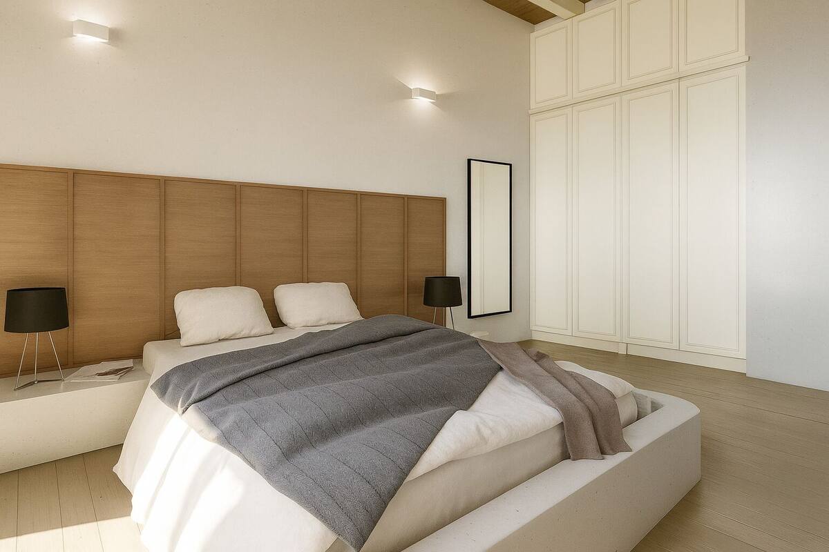 Une chambre moderne avec une tête de lit en bois, un grand lit recouvert d’une couverture grise, des lampes de chevet et une grande armoire.