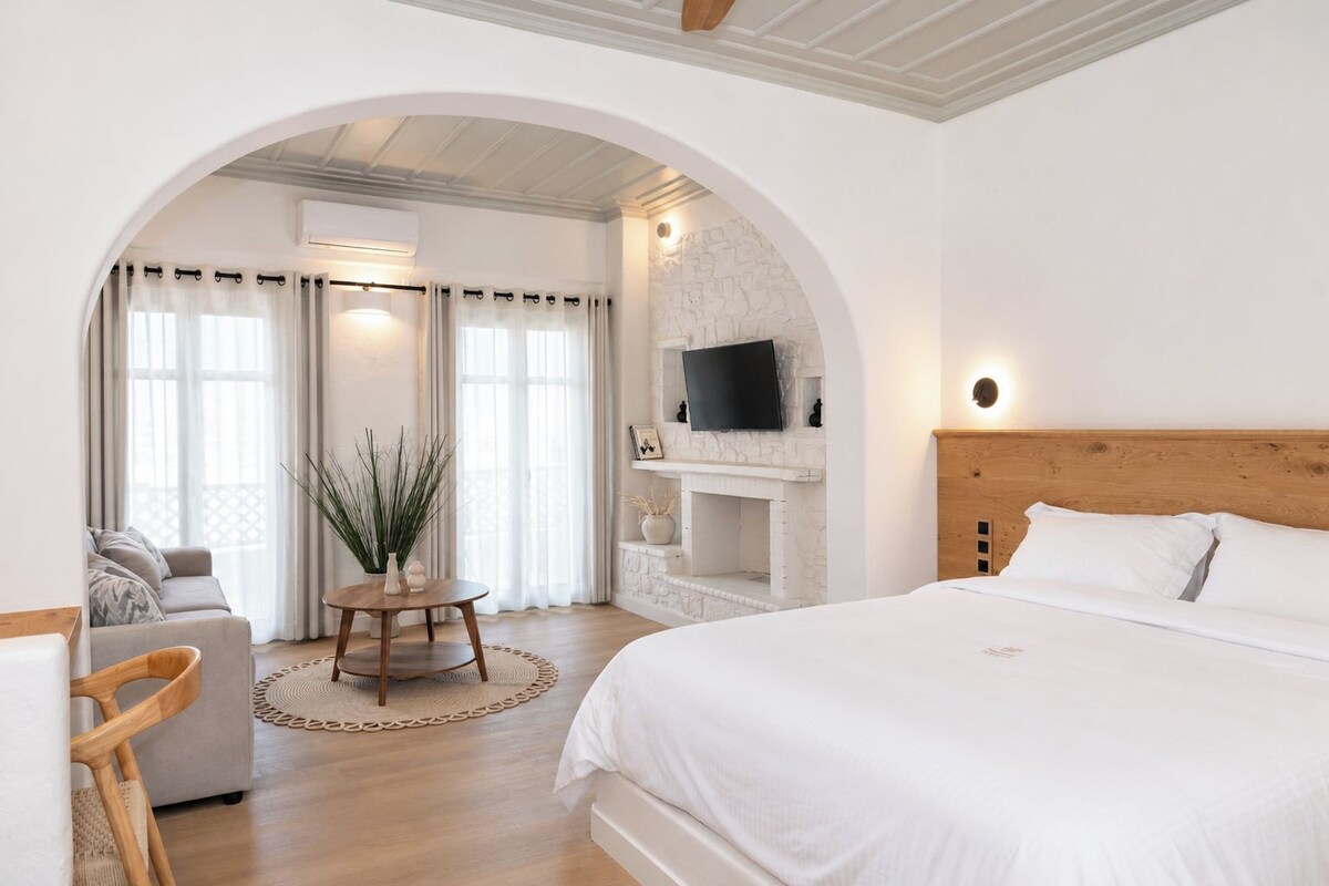 Un dormitorio moderno con una cama grande, un televisor sobre la chimenea y una zona de estar con un sofá y una mesita.