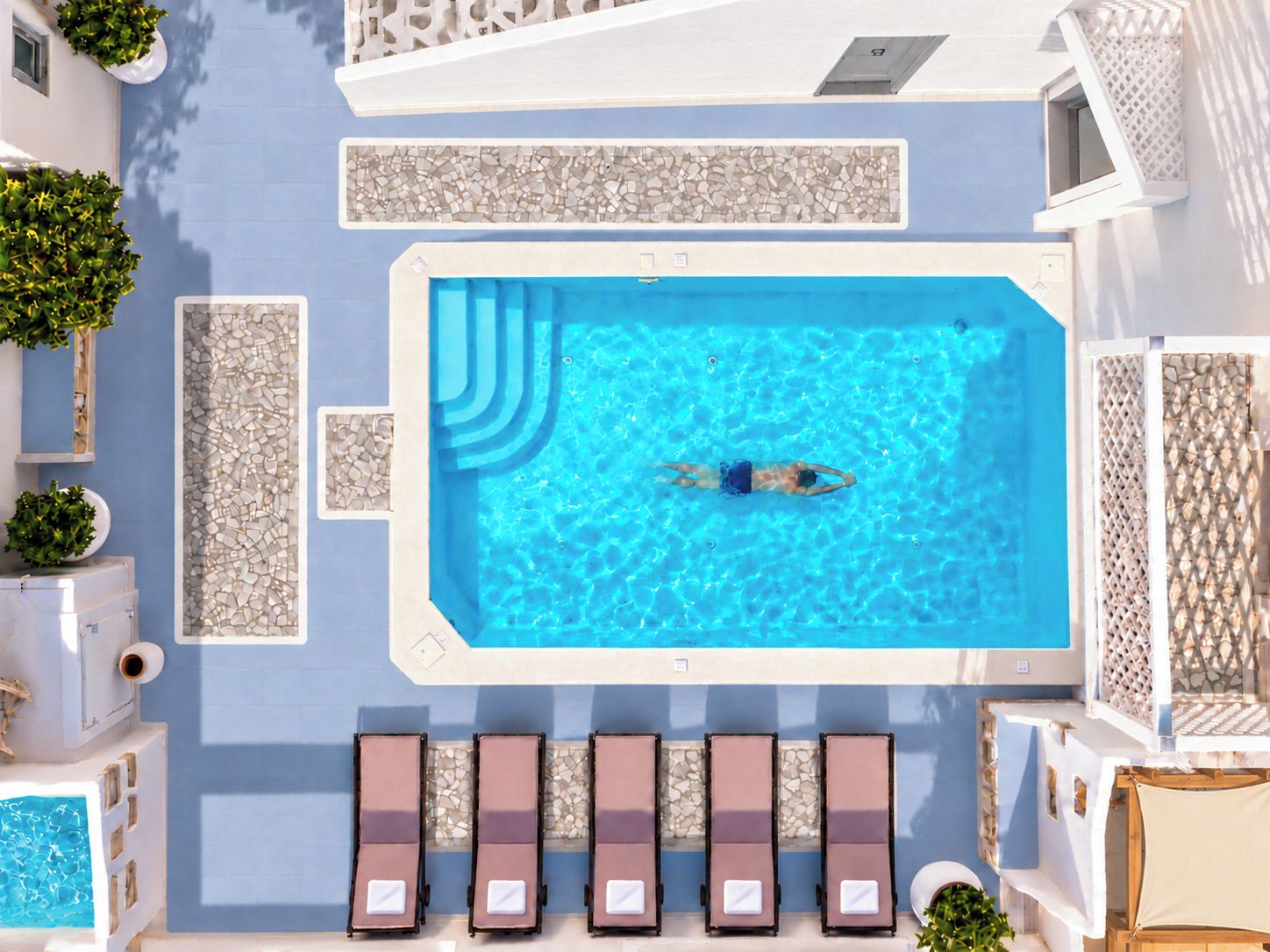 A swimming pool with a person swimming, surrounded by lounge chairs and decorative tiles.