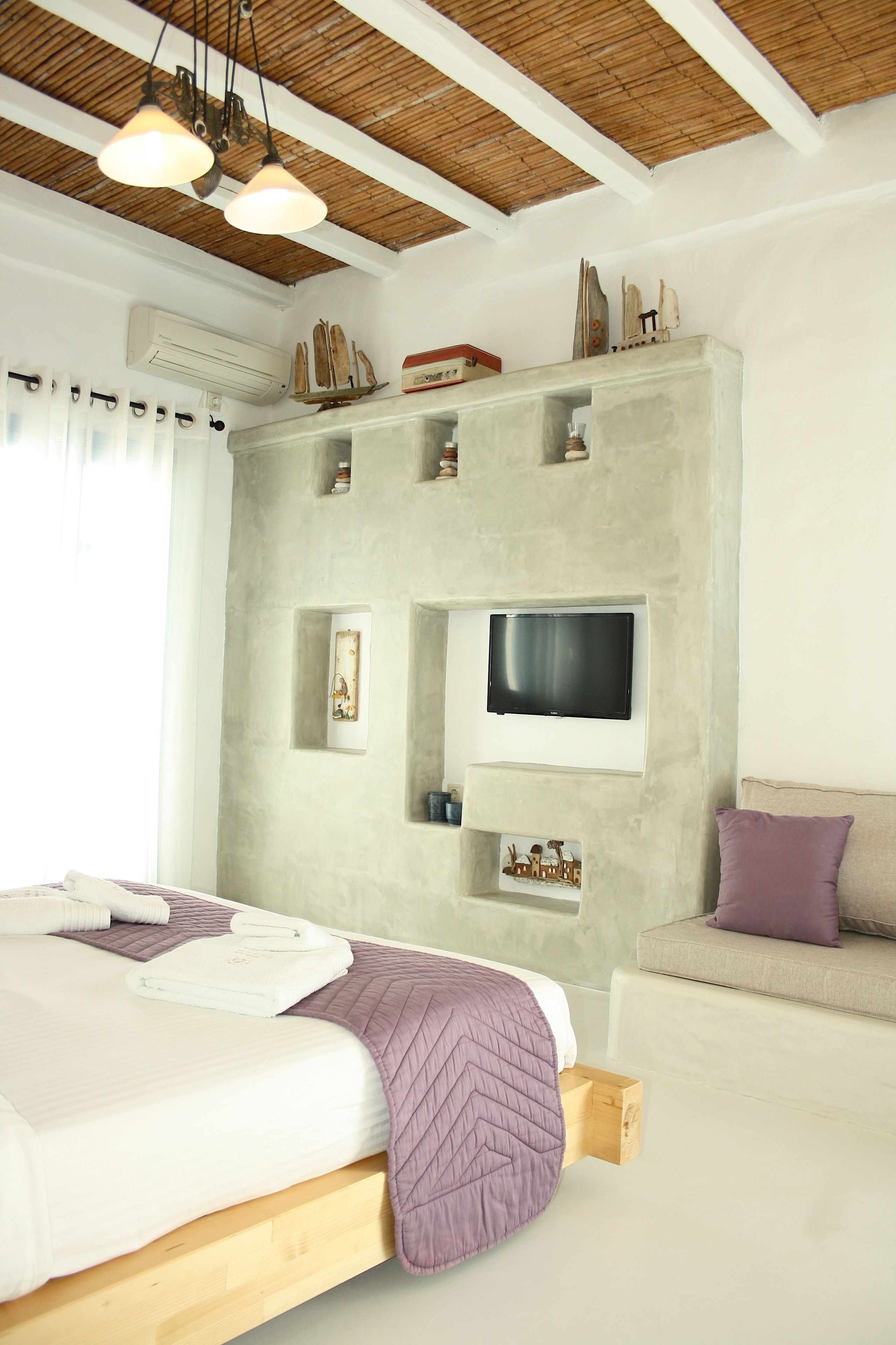 Un dormitorio moderno con cama, sofá, televisor montado en la pared y un bloque de madera debajo de la cama.