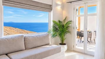 Una sala de estar con un sofá, una planta en maceta y vista al mar a través de un ventanal grande.
