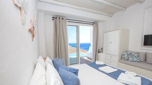 A bedroom with a bed, a TV, a sofa, and a view of the sea.