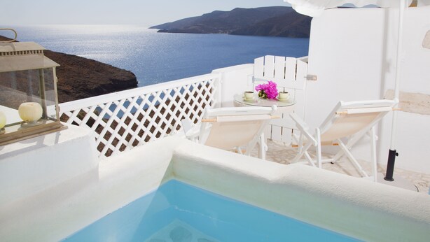 A pool area with a view of the sea, white furniture, and a small table with flowers.