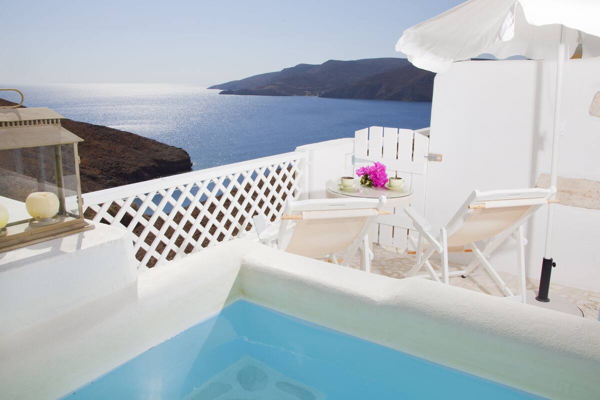 Un espace piscine avec vue sur la mer, des meubles blancs et une petite table agrémentée de fleurs.