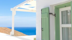 A white building with a green window and shutter, overlooking a clear blue sea.