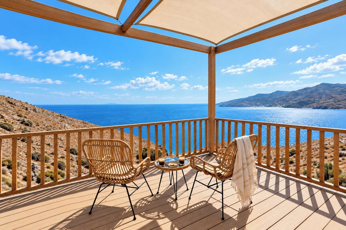 Una terraza de madera con dos sillas de mimbre y una mesa, con vistas a un paisaje costero.