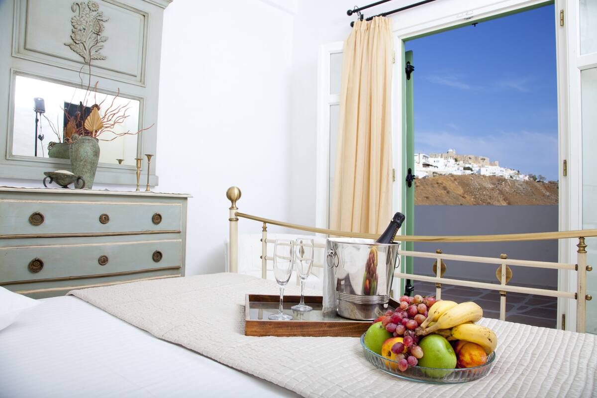 Une chambre à coucher avec un lit, une table de chevet sur laquelle se trouve un panier de fruits, un vase et une bouteille de champagne.