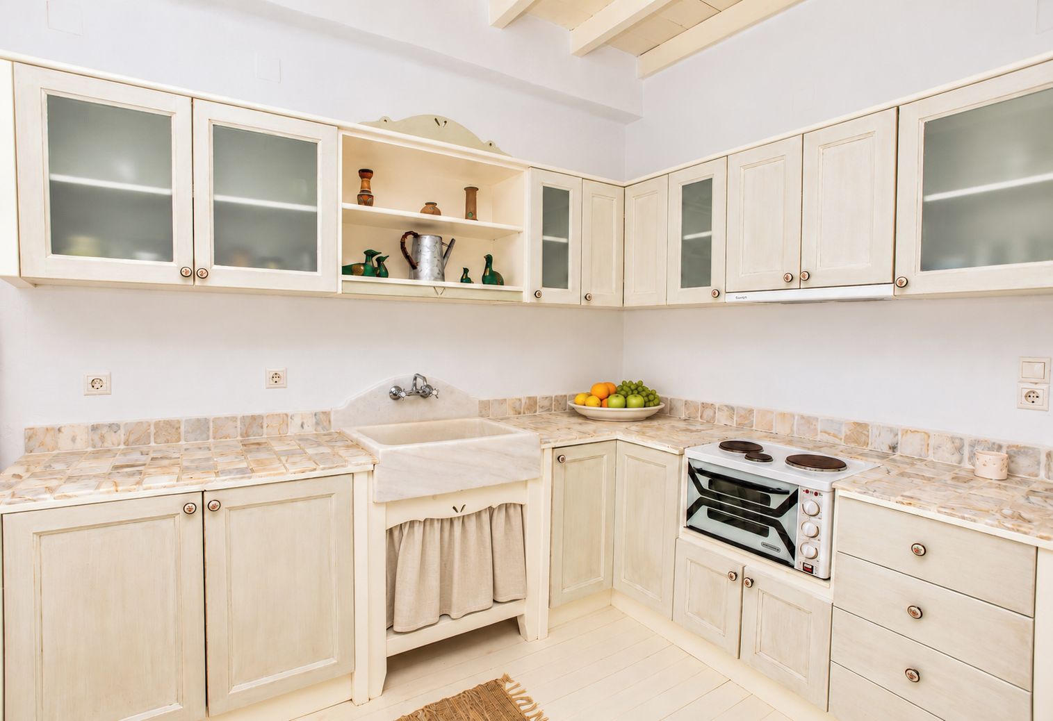 Una cocina con armarios blancos, un lavabo, una estufa y un frutero.