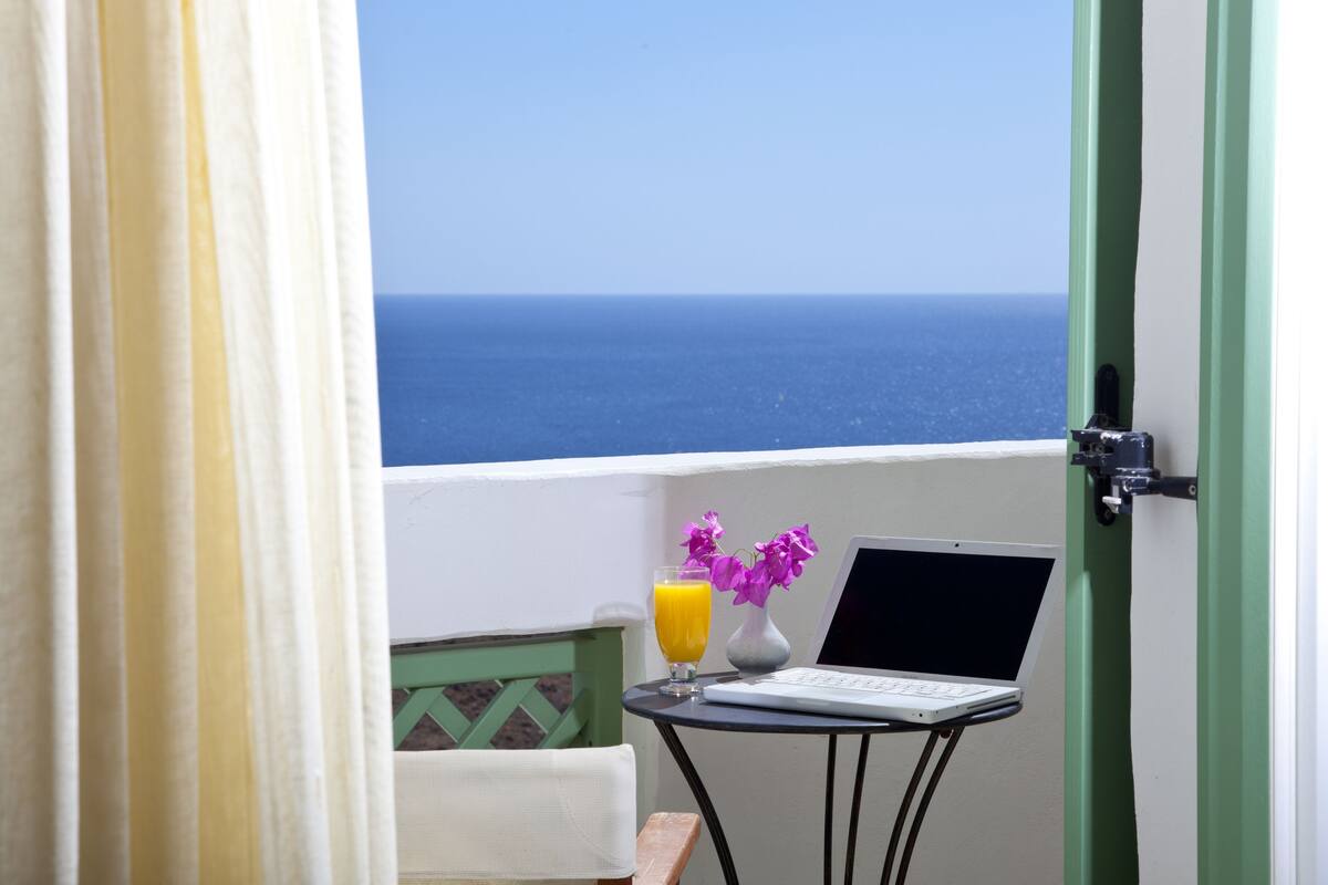 Un balcon avec un ordinateur portable, un verre de jus d’orange et des fleurs violettes.