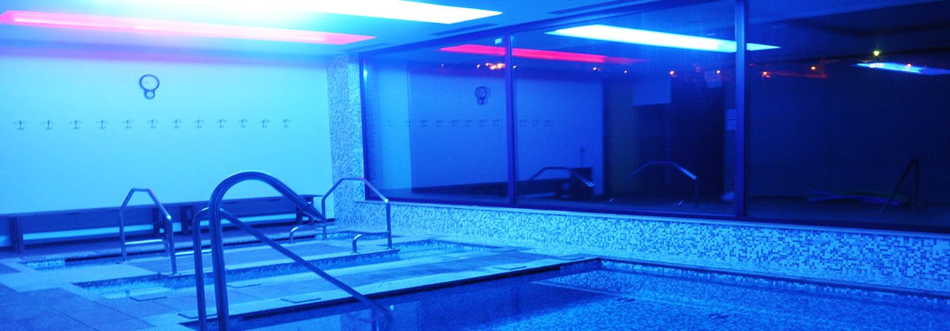 A modern indoor pool area with glass railings and a seating area.