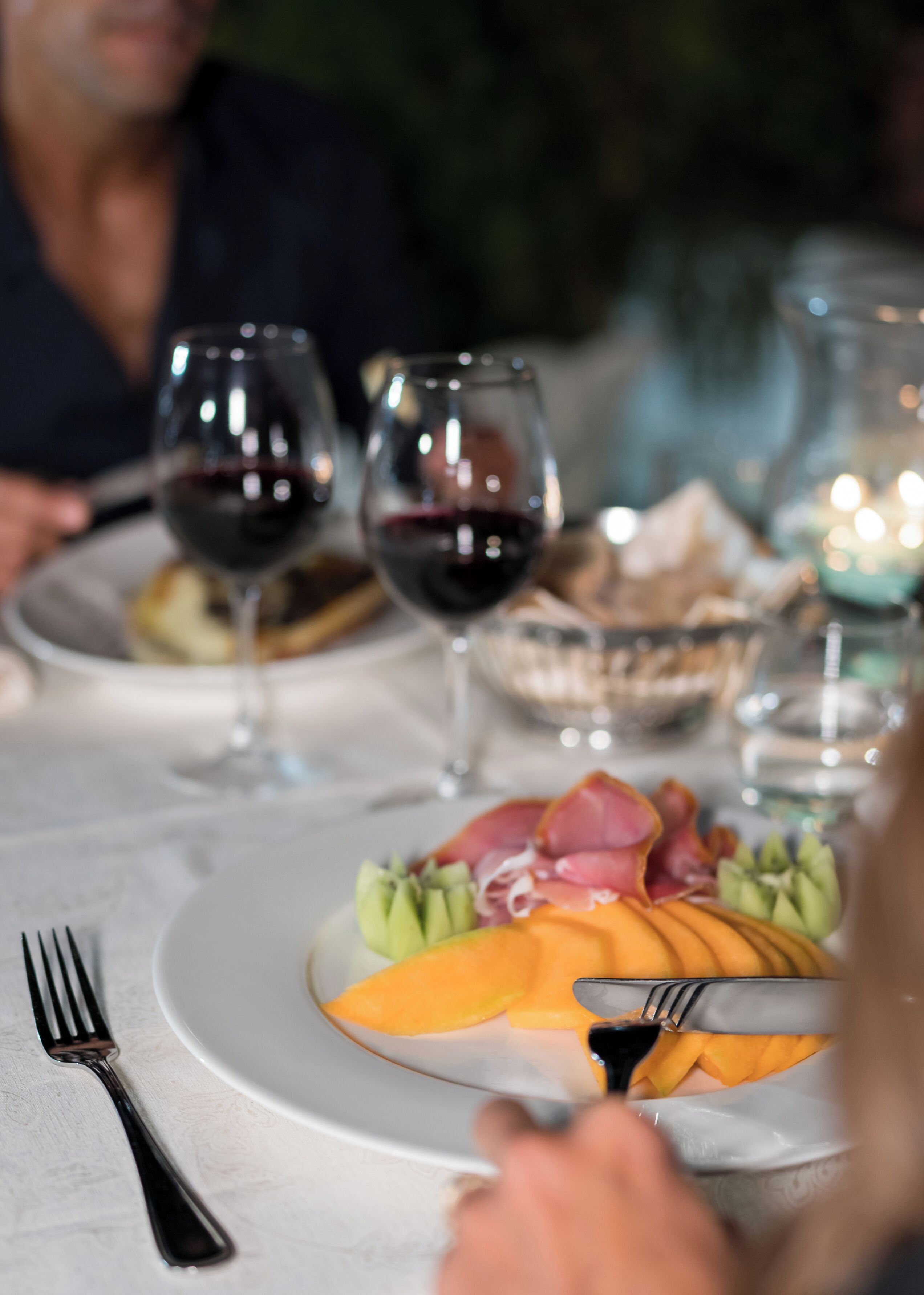 A dining table with plates of food, glasses of wine, and a fork.