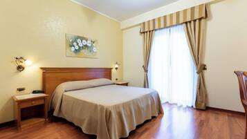 Une chambre d’hôtel avec un lit en bois, une table de chevet, un tableau au mur et une fenêtre avec des rideaux.