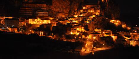 A nighttime view of a historic town with buildings illuminated against a rocky backdrop.