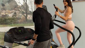 A man and a woman exercising on treadmills in a room with large windows overlooking a scenic view.