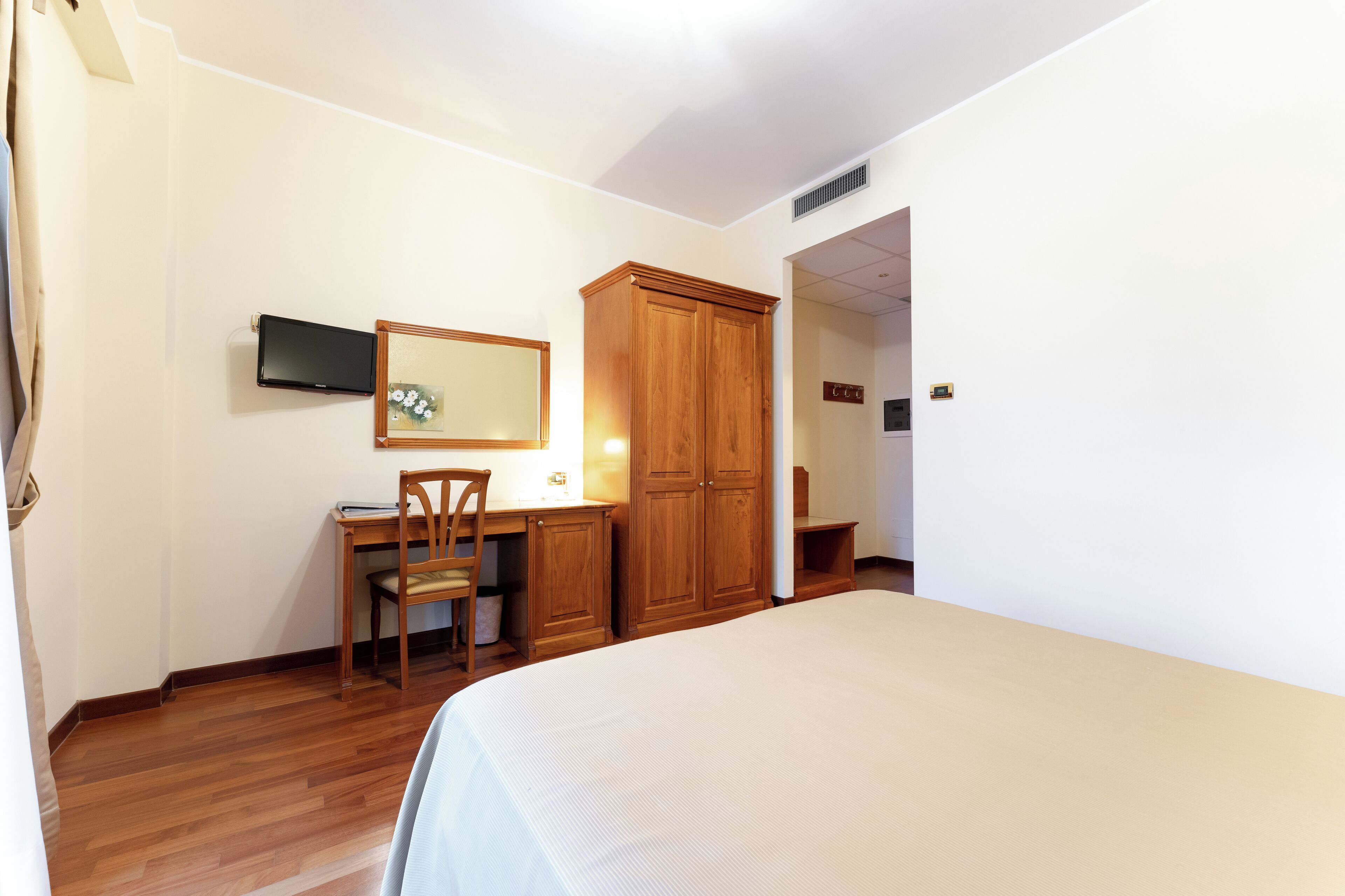 A bedroom with a bed, a desk, a chair, a wardrobe, and a television mounted on the wall.