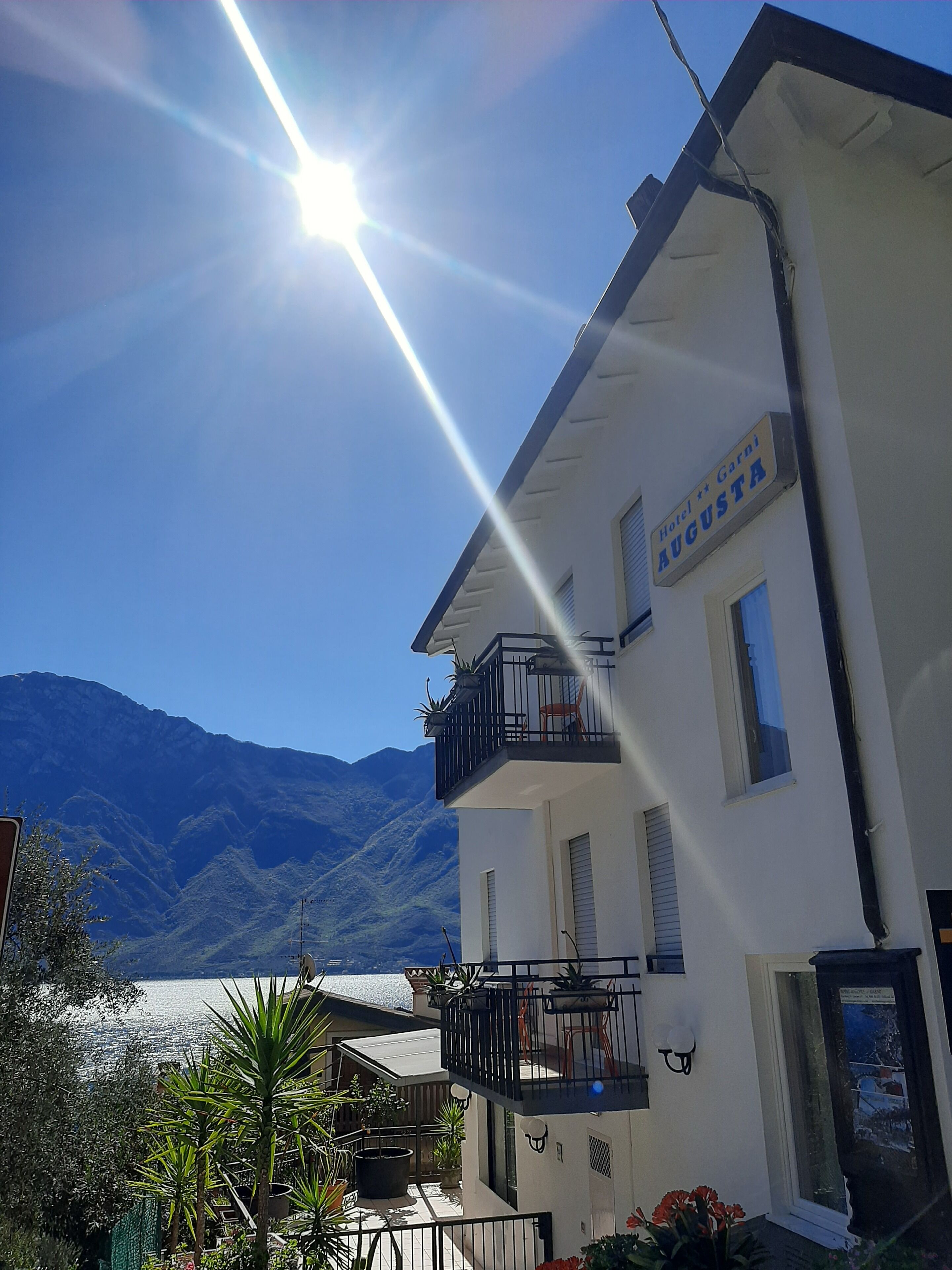 Un hôtel appelé « Hotel + Garni AUGUSTA » doté d’un balcon, offrant une vue sur les montagnes et un lac.