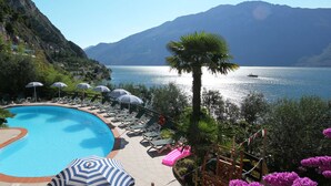 Una piscina amb gandules i ombrel·les, envoltada de muntanyes i una massa d'aigua.