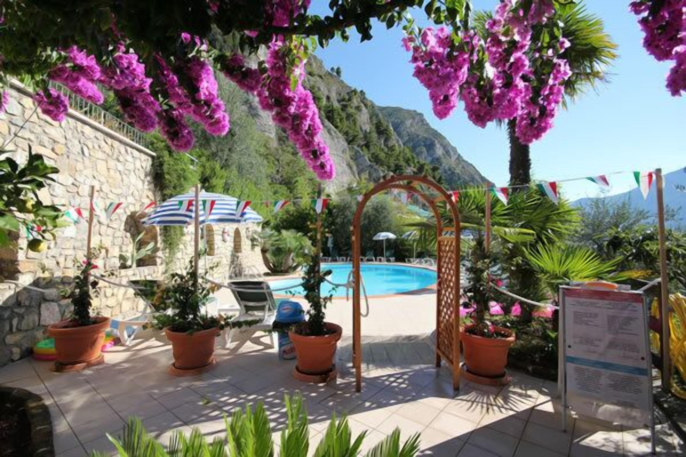 Ein Poolbereich mit Pergola, Blumentöpfen und einer Steinmauer.