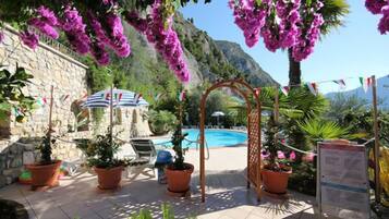Ein Poolbereich mit Pergola, Blumentöpfen und einer Steinmauer.