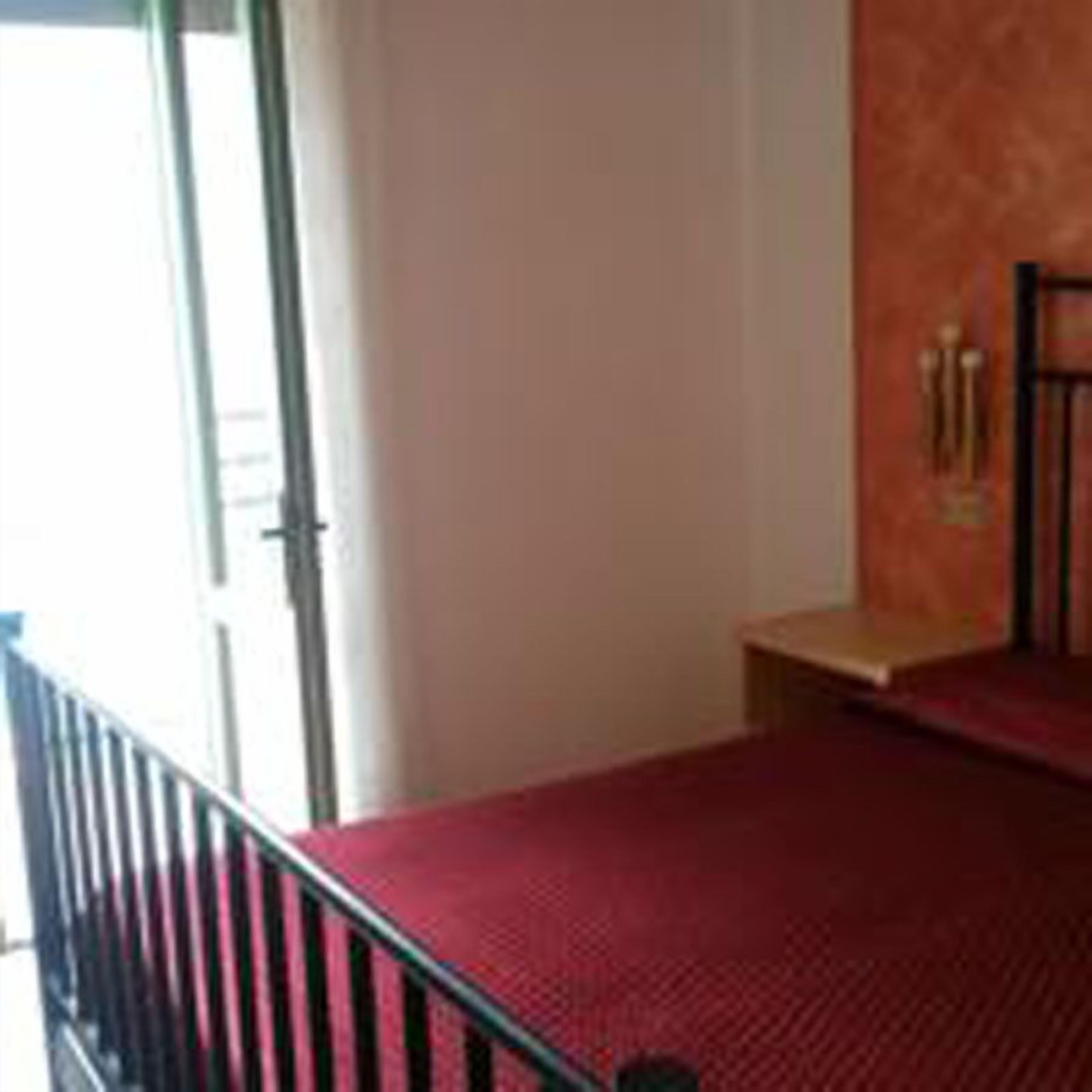 Una habitación con alfombra roja, una pequeña mesa de madera y una barandilla de metal negro.