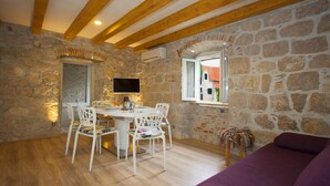 Ein rustikaler Raum mit Steinwänden, Holzbalken, einem Esstisch mit Stühlen, einem Flachbildfernseher und einem violetten Sofa.