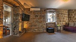 Ein Zimmer mit Stehwänden, einem Fernseher, einem Fenster, einer Couch und einem kleinen Tisch mit Obst.