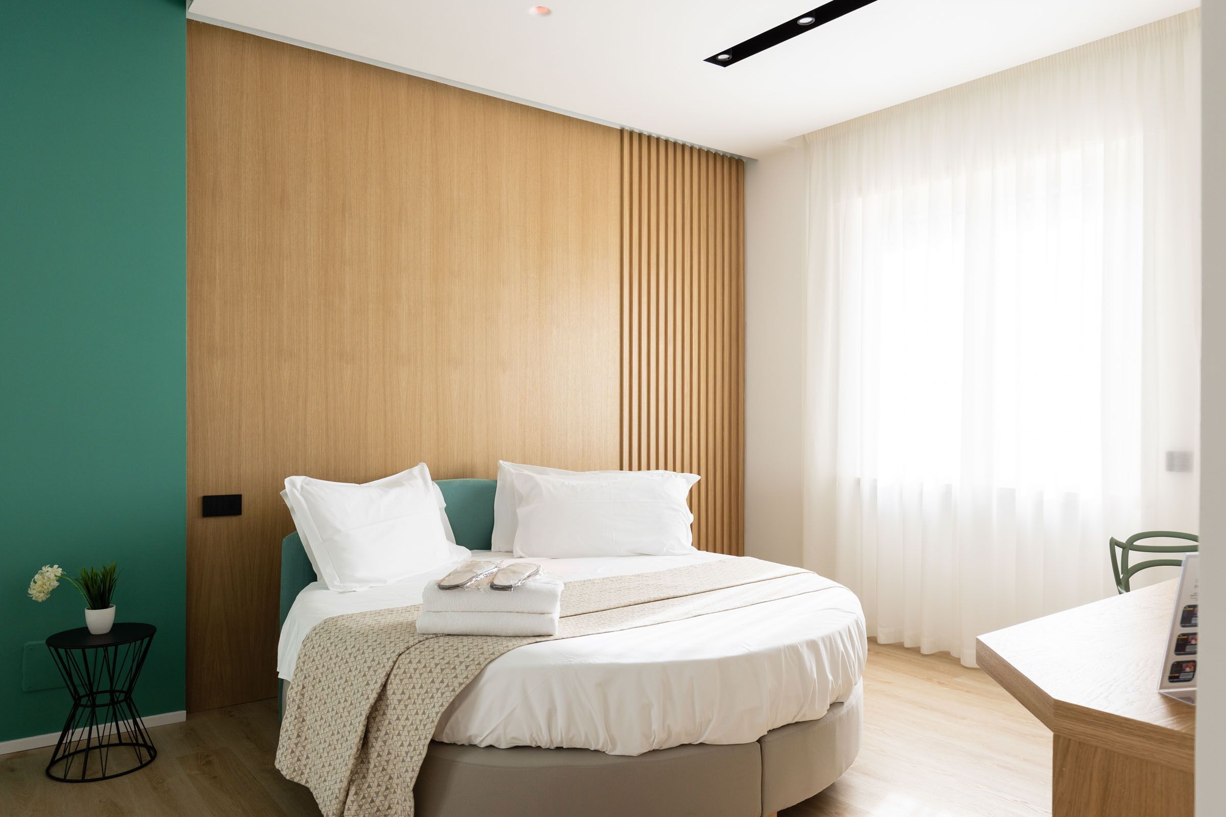 A modern bedroom with a bed, a small table with a plant, and a desk with a chair.
