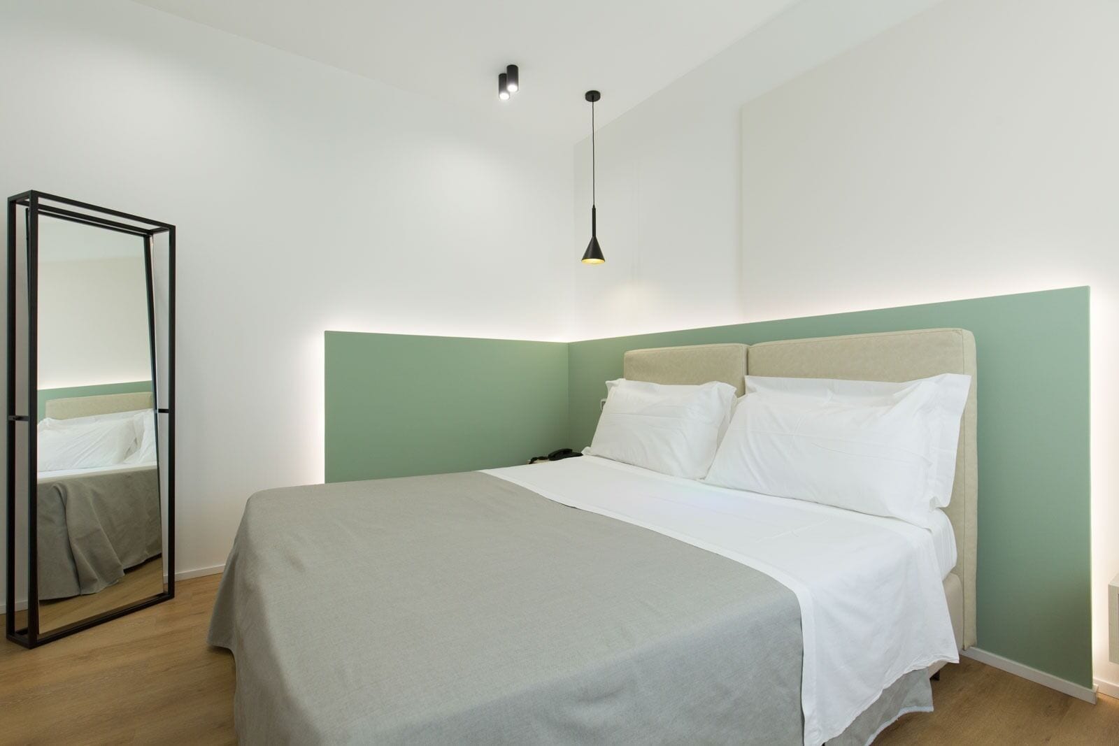 A bedroom with a bed, a mirror, and a hanging light fixture.