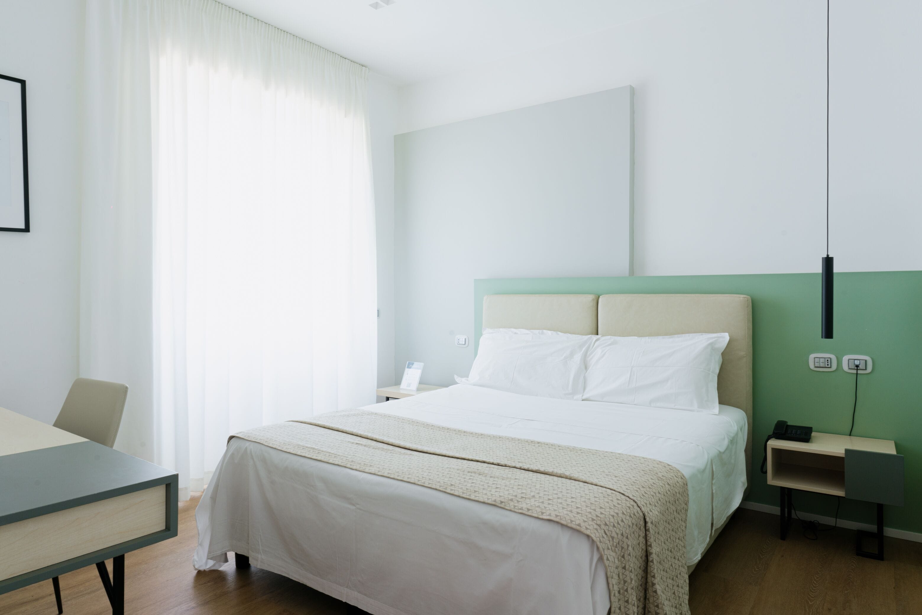 A hotel room with a bed, a desk, a chair, and a nightstand.