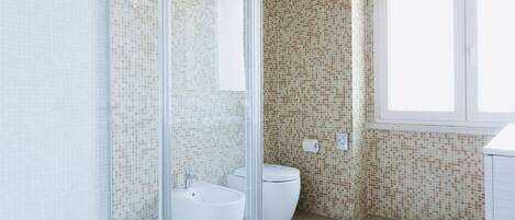 A bathroom with a glass shower enclosure, a toilet, and a bidet.