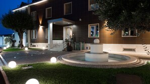 A modern building with a well-lit entrance, a central fountain, and a landscaped garden. - Hotel Plana (Caserta)