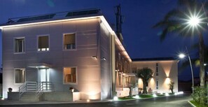 A modern hotel with a flat facade, multiple windows, and a well-lit entrance. - Hotel Plana (Caserta)