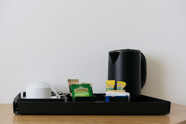 Una bandeja con una cafetera negra, un hervidor blanco y sobres de té Twinings y café Miele.